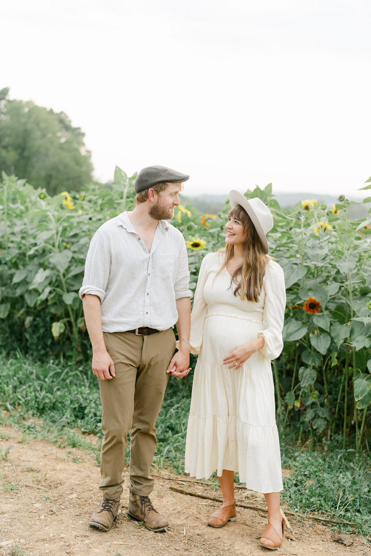 pregnant women holds husband's hands in a field of sunflowers.