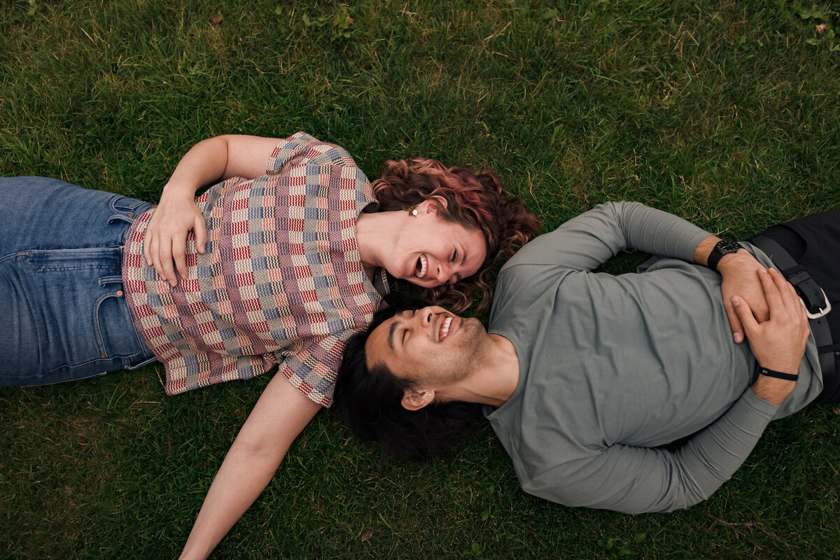 A couple laughs while  laying on the ground