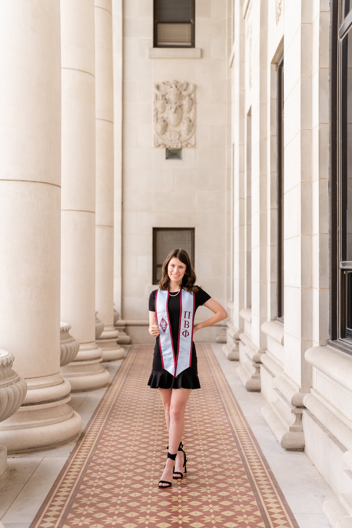 Texas A&M senior girl smiling and wearing a black dress and Pi Phi stole with hand on hip and thumbs up in columns of the Administration Building