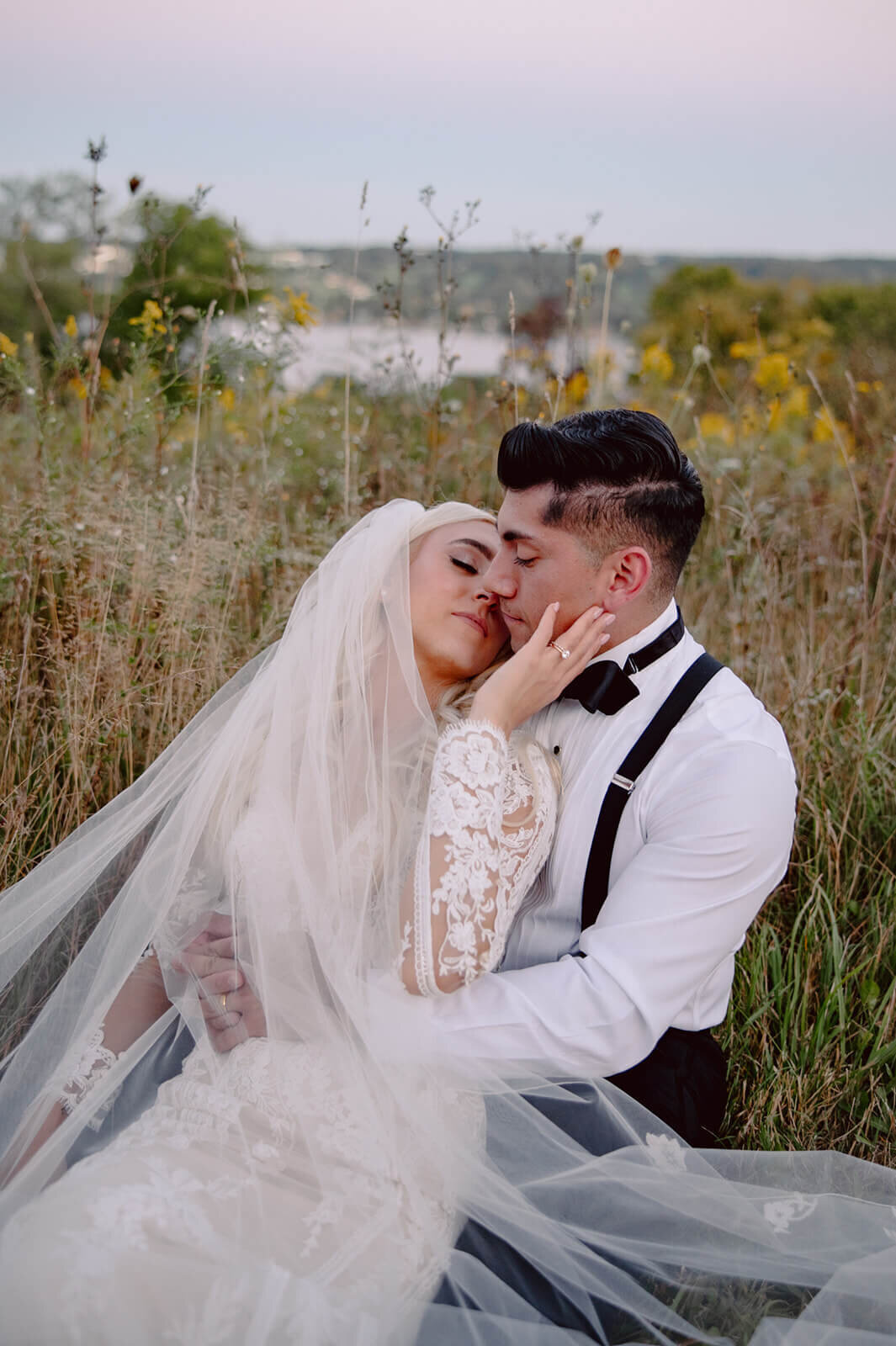 Bride and groom sitting in field with bride leaning back to kiss groom at Finger Lakes wedding at Crispin Hill on Keuka Lake