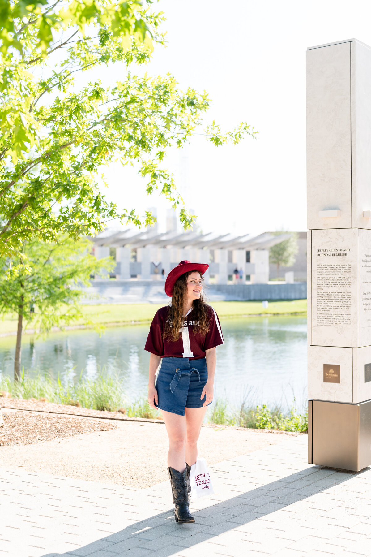 Texas A&M senior girl walking and laughing away while wearing maroon cowboy hat, jersey, boots and jean skirt in Aggie Park
