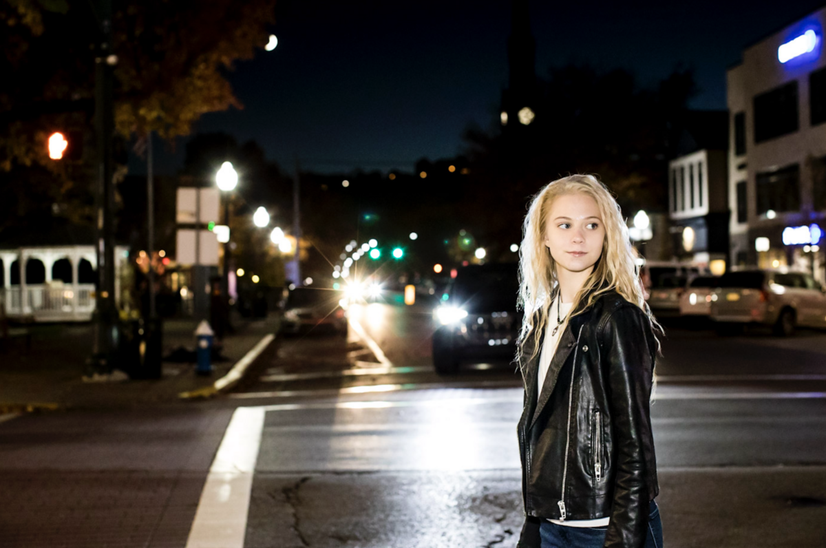 A blonde senior girl walks across the street at night in the village of Sewickely.
