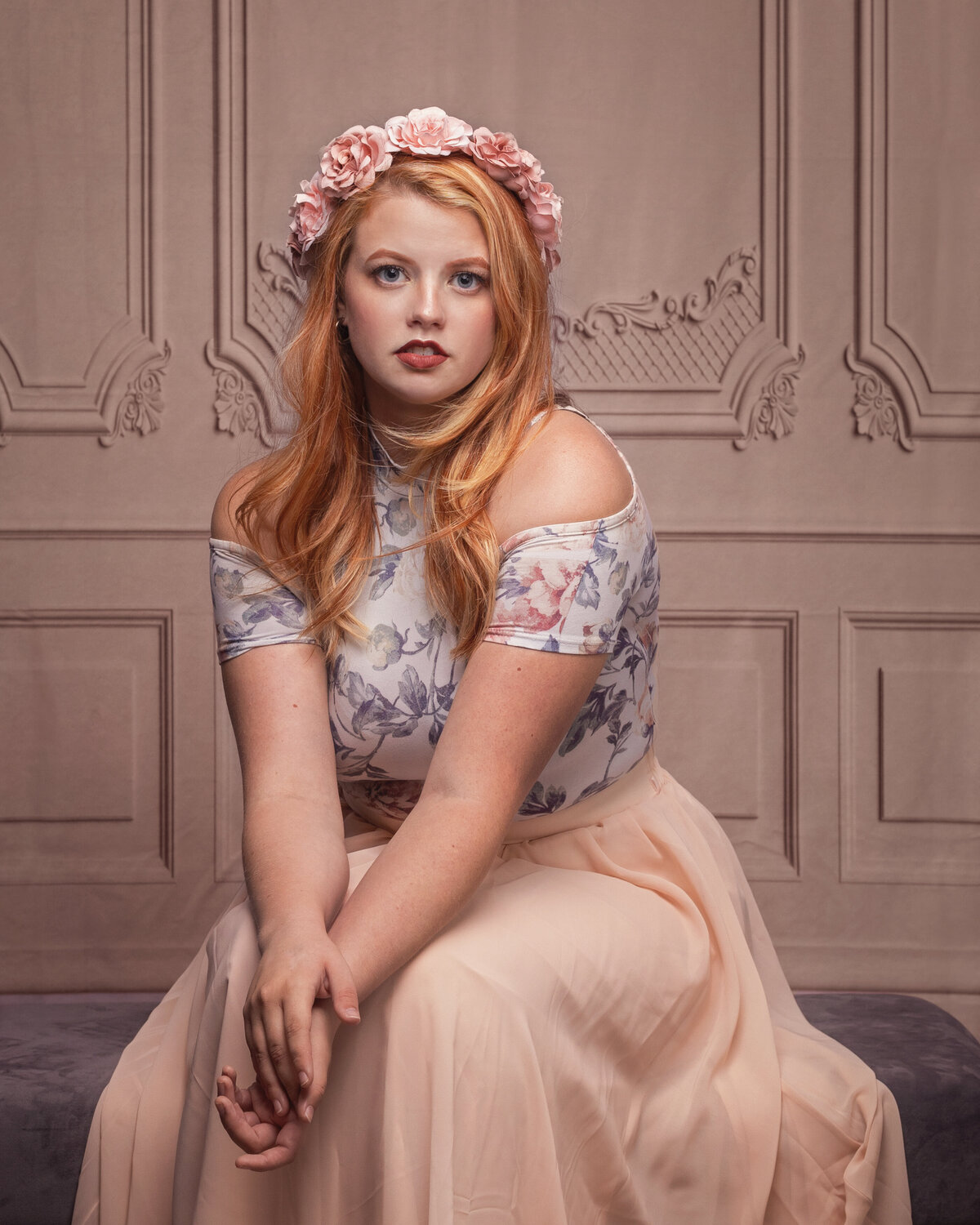 orange haired girl sitting in a beautiful studio facing forward with hands together