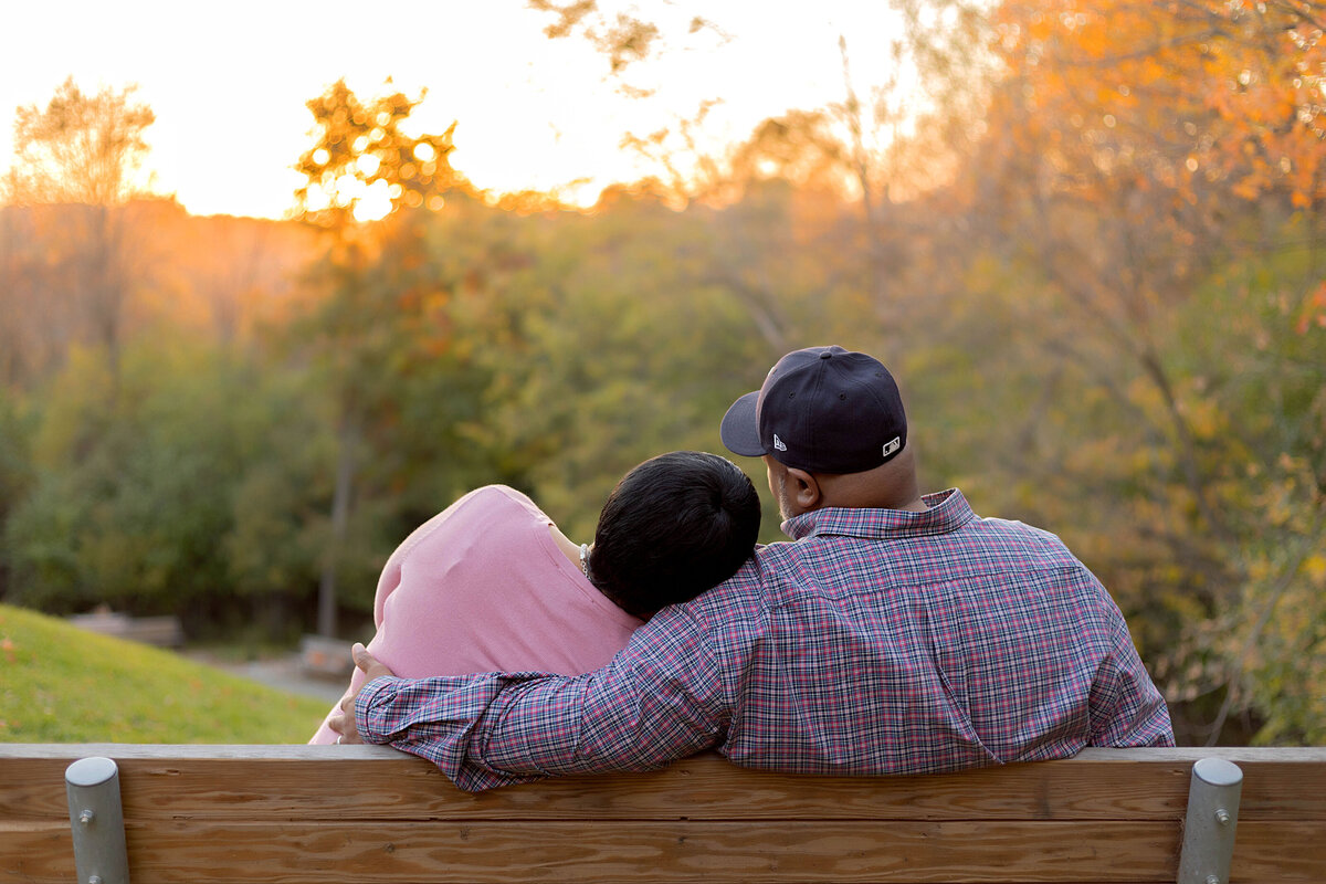 Husband and wife sitting on bench looking at the sunset