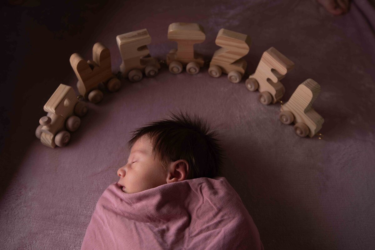 a baby is swaddled in a mauve blanket with her name in wood blocks surrounding her