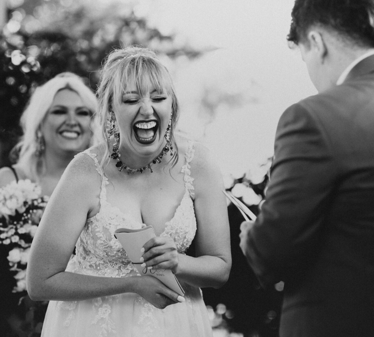 Bride laughing heartily during the wedding ceremony with the officiant and bridesmaid smiling in the background