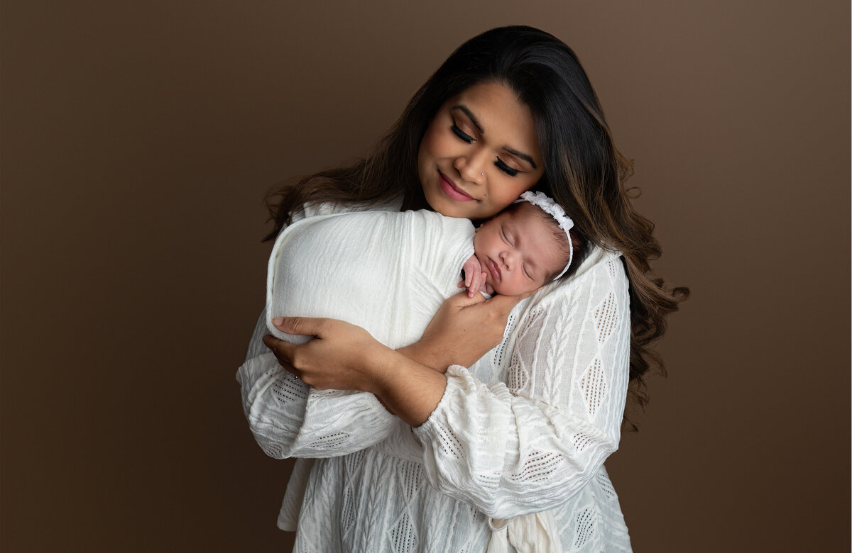 Studio portrait of a mother gently cradling her newborn baby, wrapped in soft white and captured in Paris, Ontario. A heartfelt addition to the Family Portfolio at Meraki Photographic Creations.