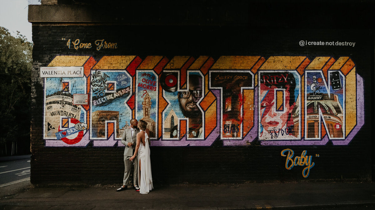 A bride and groom kiss in front of the Brixton mural on their wedding day.