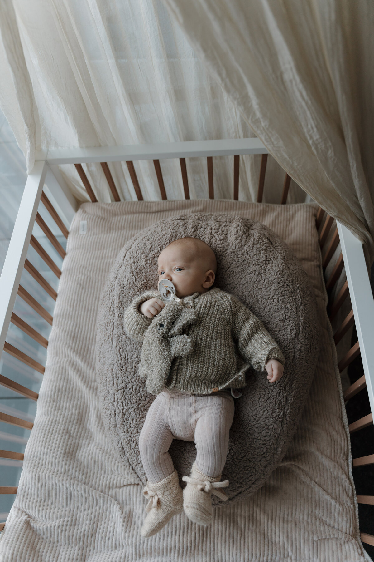 Newborn baby ligt in wiegje met tut en wollen trui.