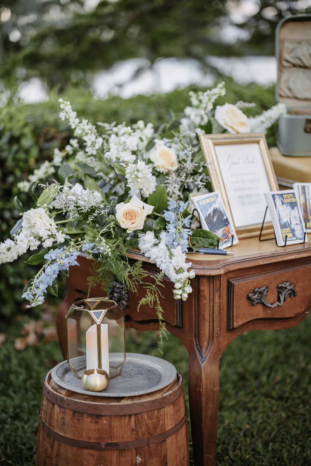 Wedding welcome trunk sititng on antique table surrounded by greenery and shrubs