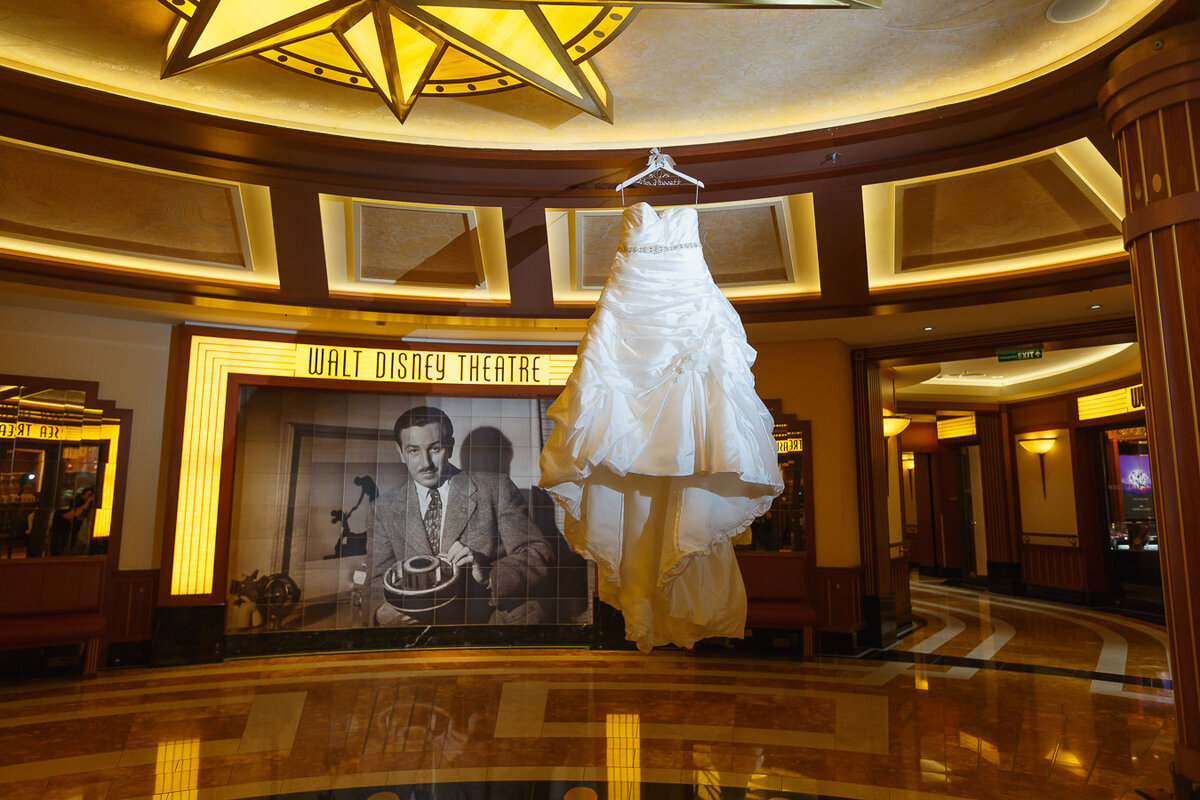 Wedding dress hanging in front of walt Disney theater sign with photo of Walt Disney on Disney Dream