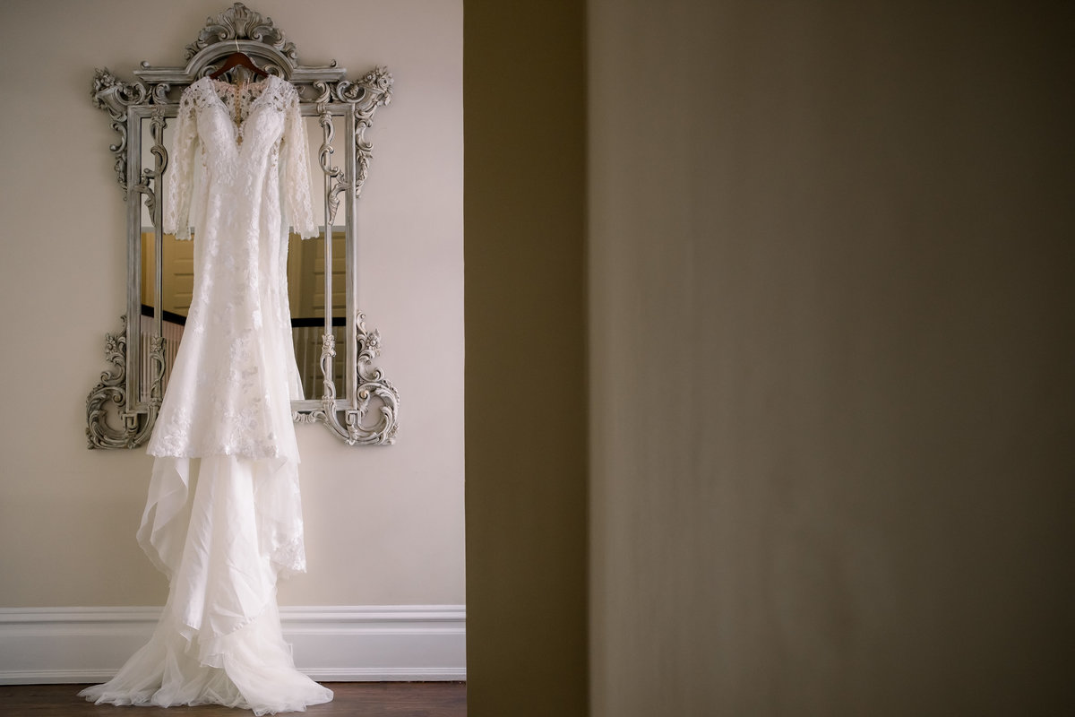 Beautiful art deco inspired wedding dress hangs on an ornate mirror before the wedding ceremony at the orlo in Tampa, Fl