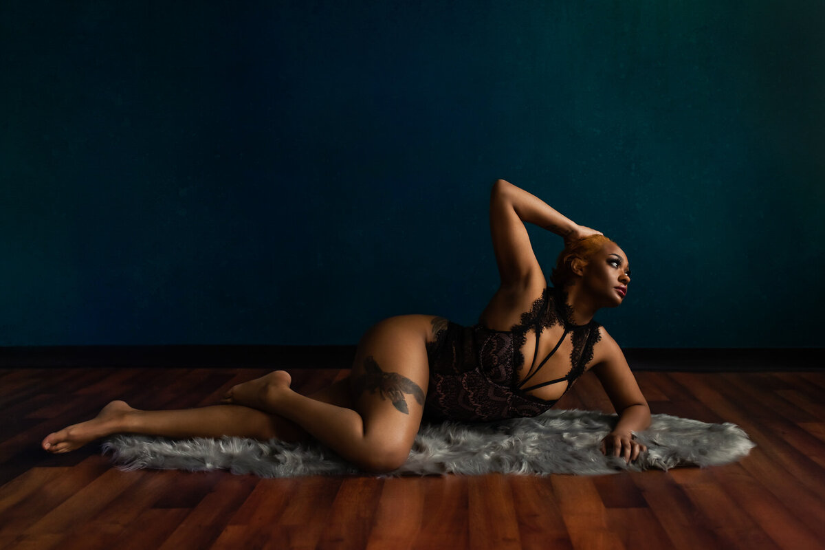 Woman poses lying on a rug in front of a teal wall