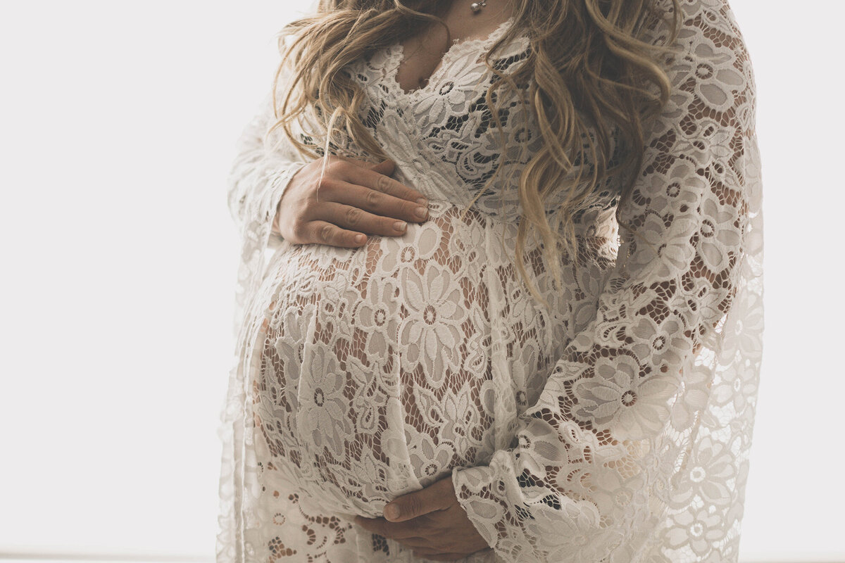 Details of a pregnancy bump in a white lace maternity gown
