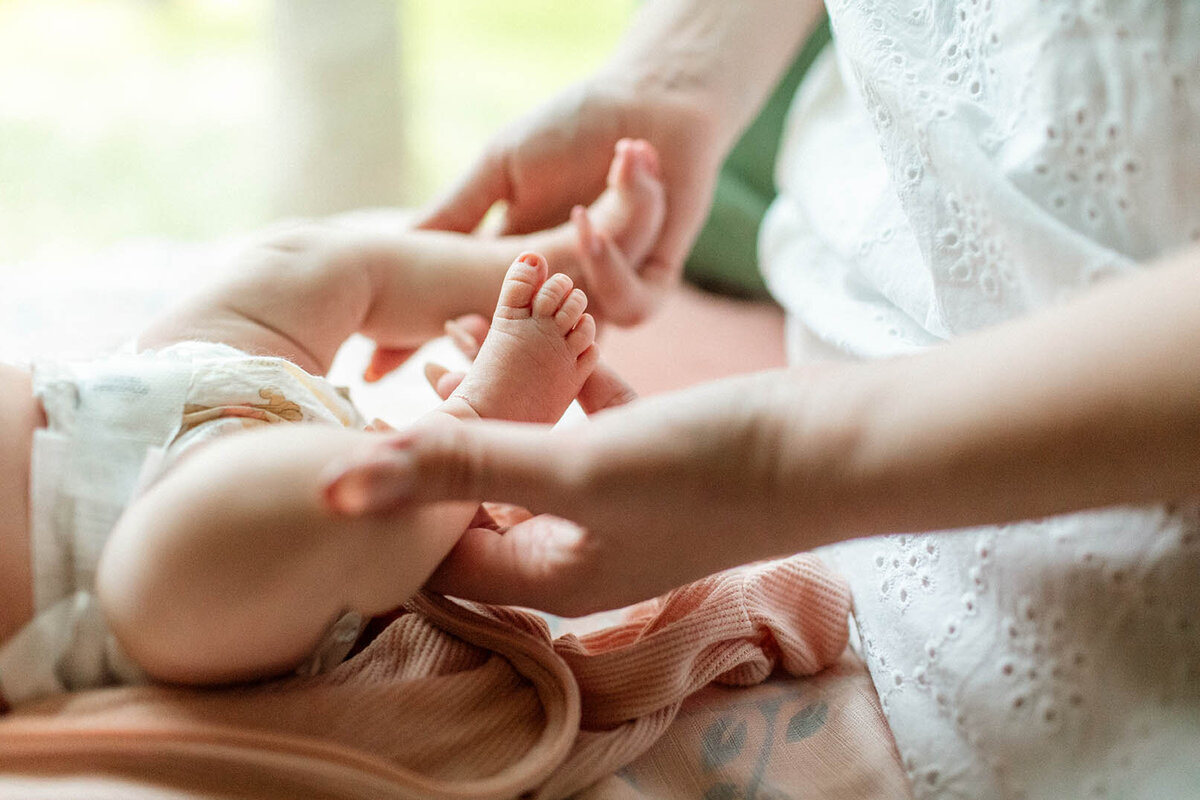 Mother gently holding baby's tiny feet - Sara James documents tender maternal moments and precious newborn details during loving parent-infant sessions in San Antonio Texas homes