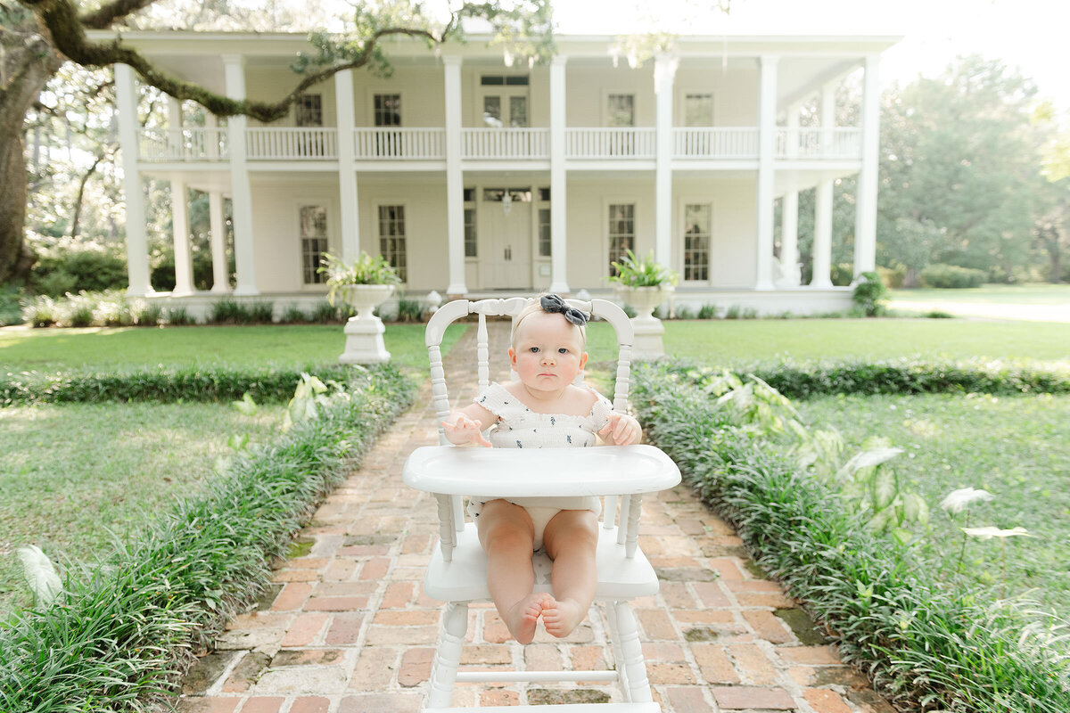 A baby girl in a high chair captured by a destin family photographer in front of a white house.