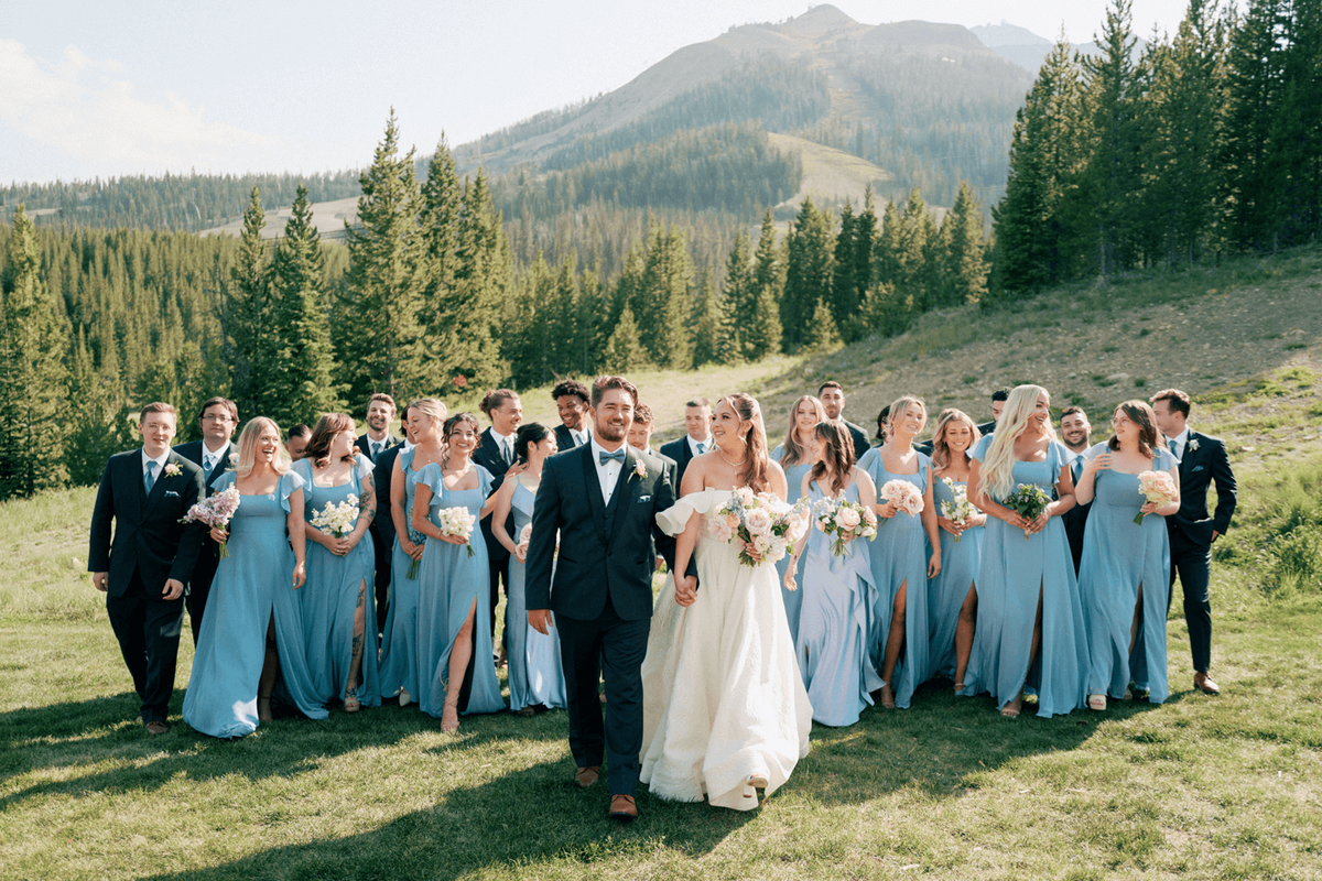 Bride and groom walking with their wedding party at a pastel summer wedding at Moonlight Basin, surrounded by friends in blue dresses and navy suits.