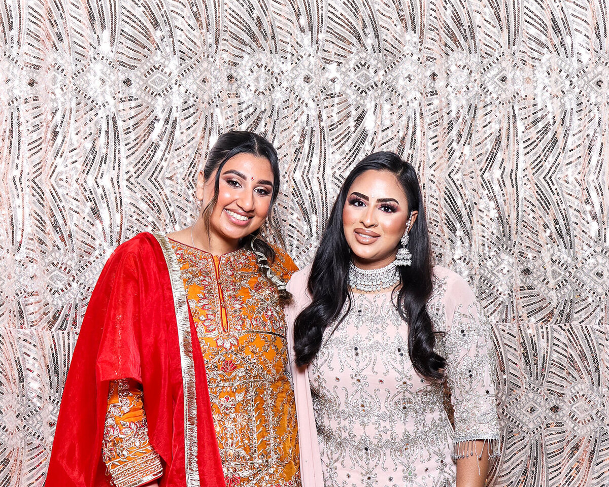 Two beautiful Asian ladies, posing against a photo booth backdrop during a large family celebration with Mad Hat Photo Booth.