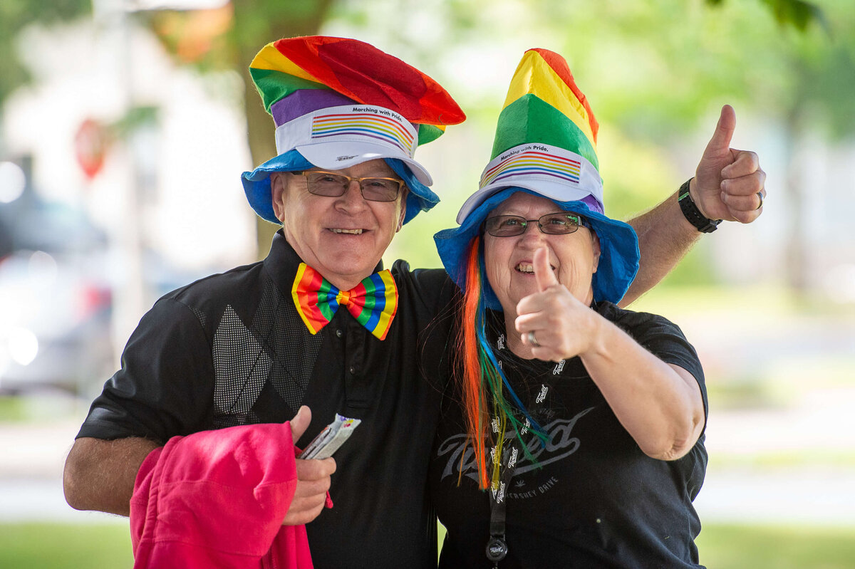 a mand and woman wearing pride clothing and hats smiling and laughing.  Captured by Ottawa Event Photographer JEMMAN Photography COMMERCIAL during the Tweed Canopy Growth Pride Parade