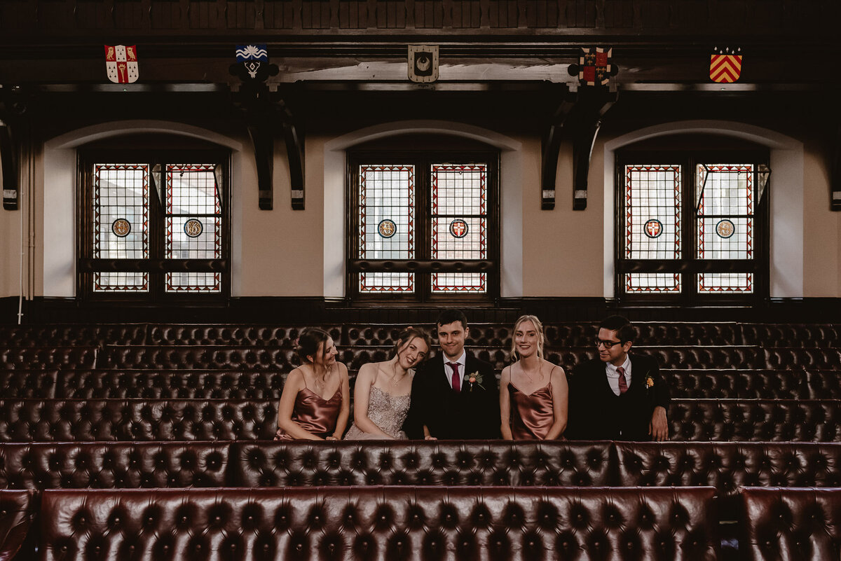 bride and groom sitting with the wedding party in the debate chamber at the cambridge union