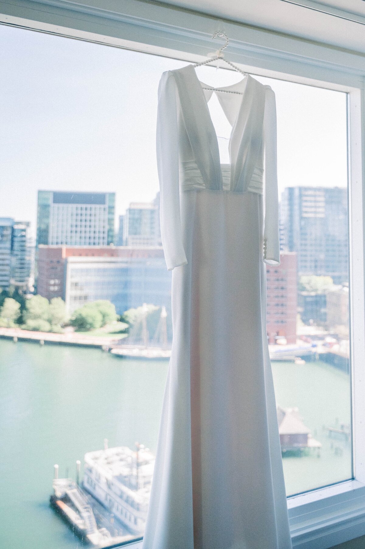 a wedding dress hanging by a window overlooking a harbor
