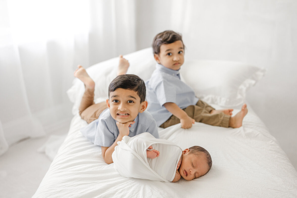 Older sibling cuddling newborn baby on white bed in light-filled Tampa studio