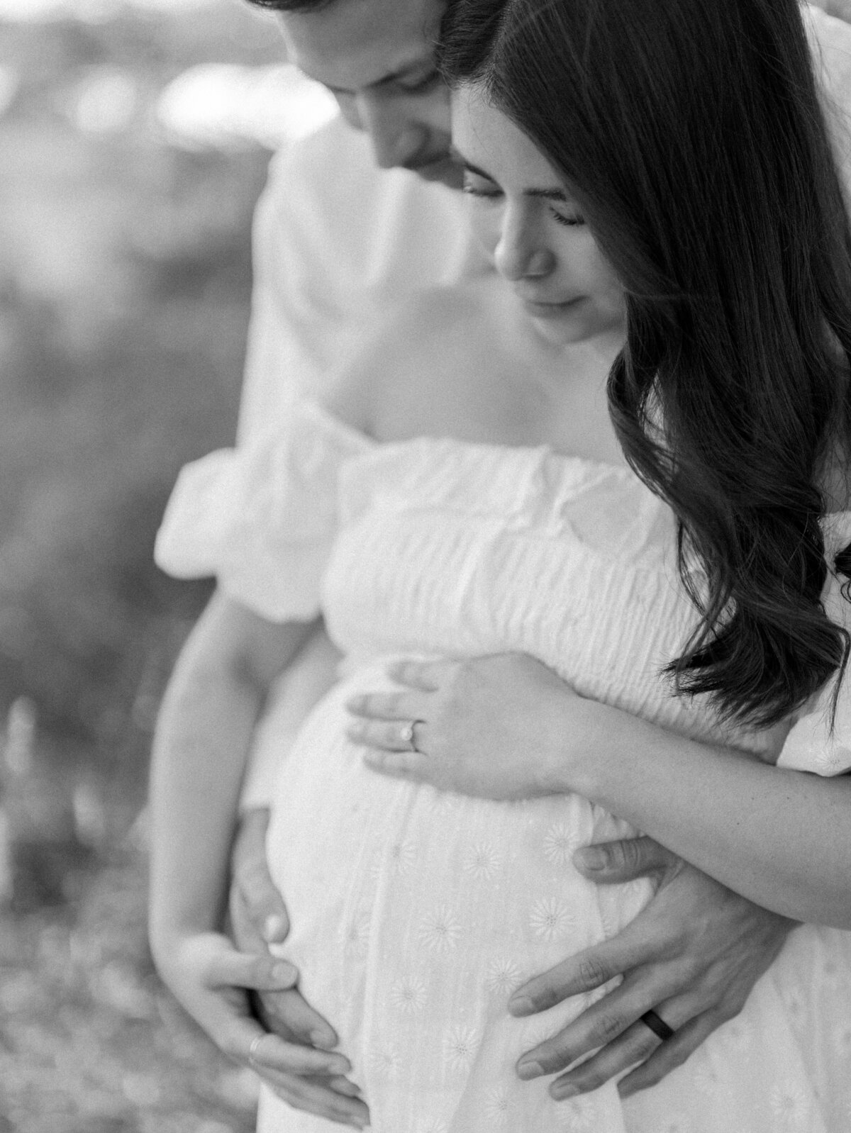 Black and white photo of husband and wife with their arms around her pregnant belly