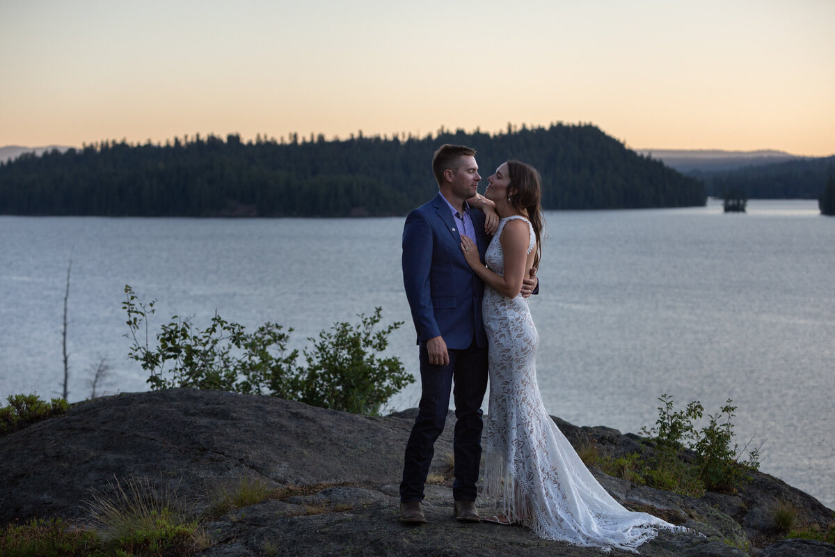 A bride and groom stand on a hill above a lake in Idaho on their wedding day.