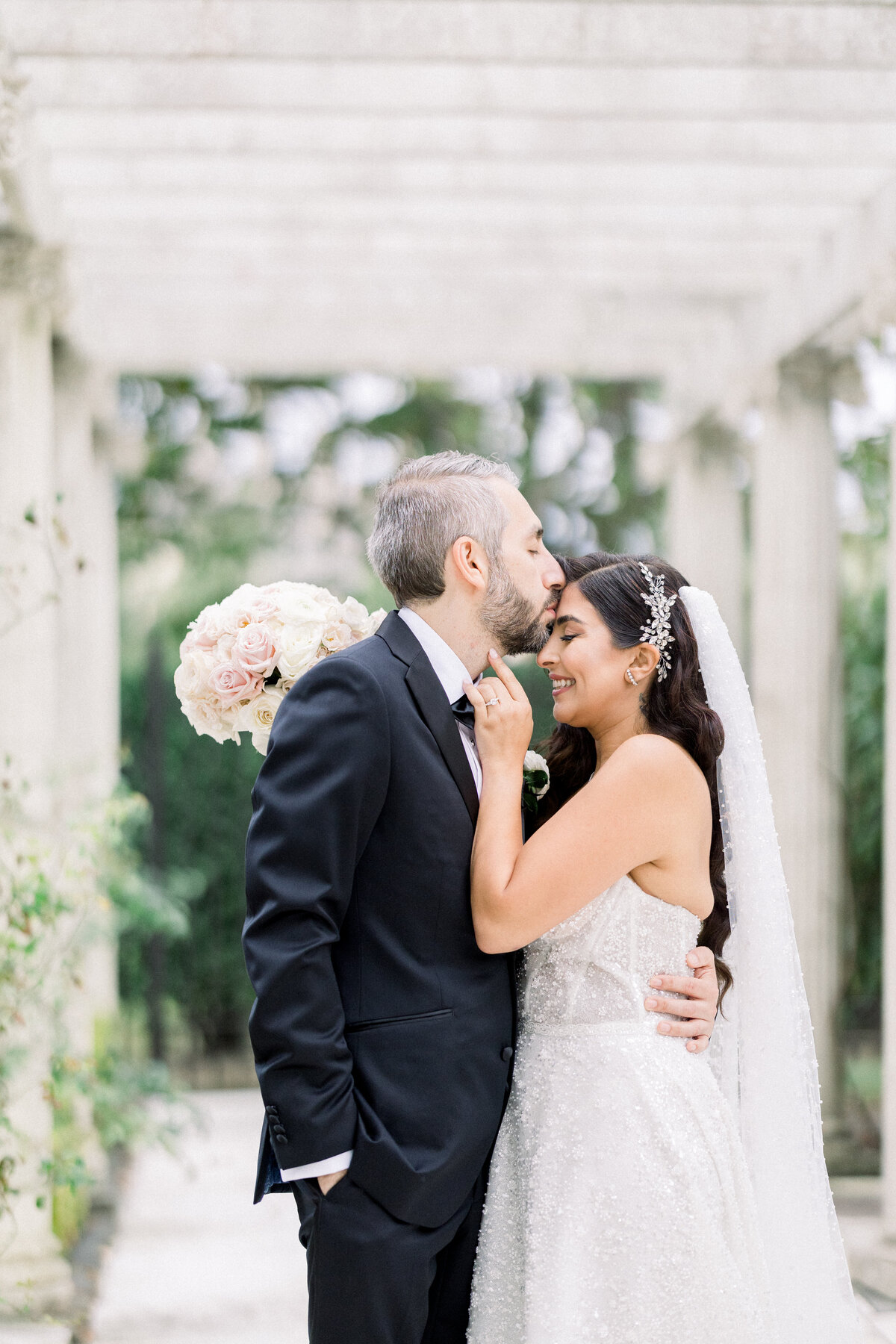 bride and groom walk through the gardens of rosecliff mansion in newport rhode island, groom kisses bride on forehead
