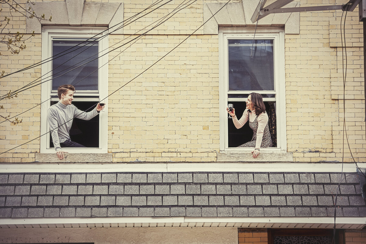 Two people holding glasses out from two different windows