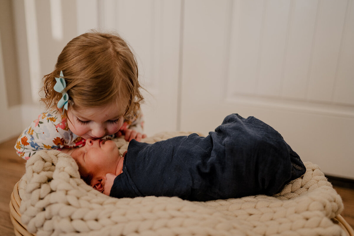 Older sibling kisses newborn during Loveland Newborn Photos