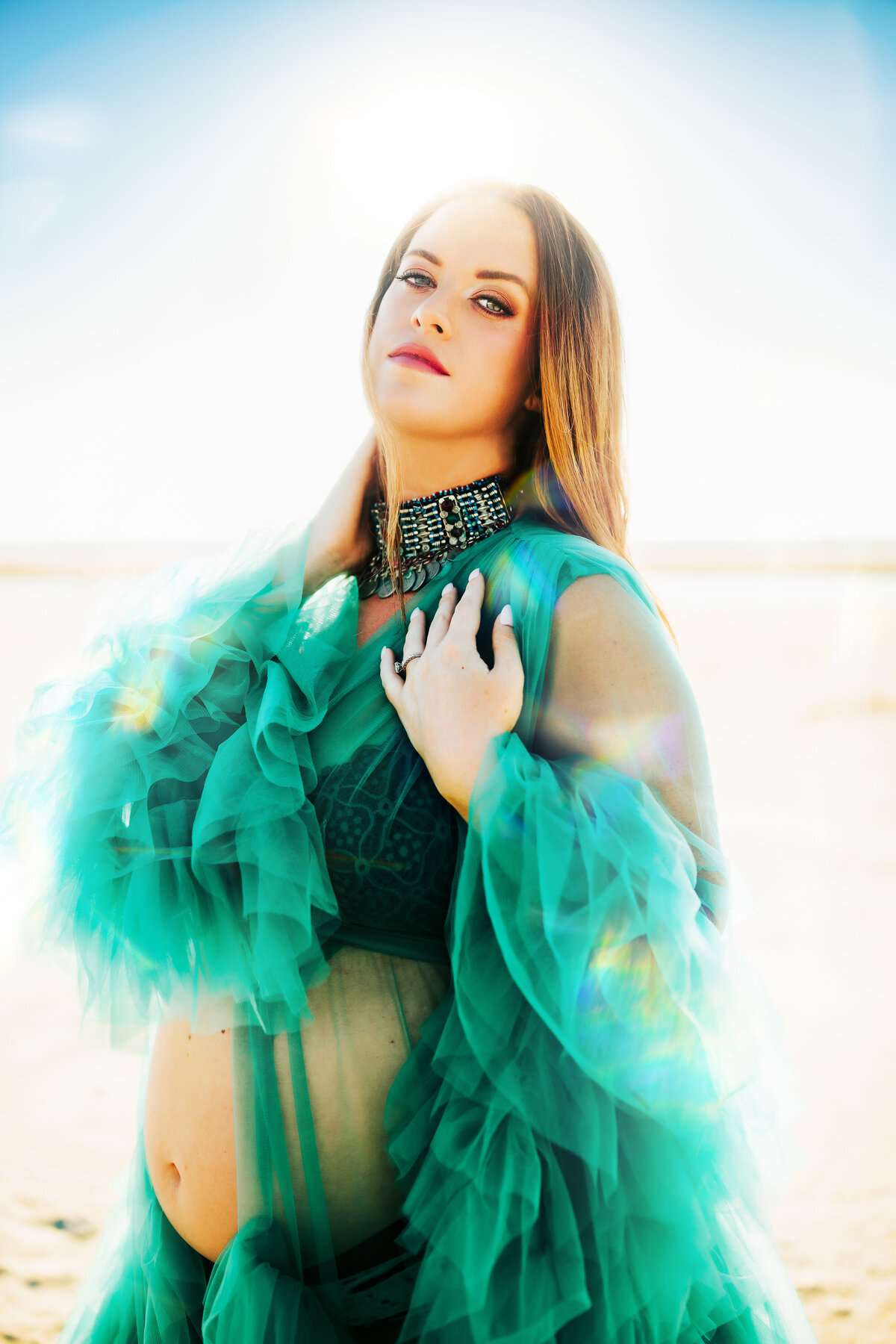 editorial portrait of a pregnant  women in a green tulle robe with her baby bump out at the beach in fl