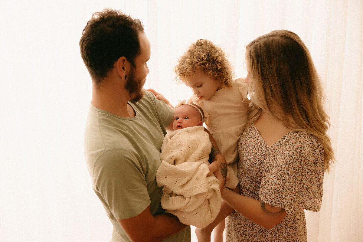 Parents and toddler sister admiring newborn during Nashville TN studio photo session