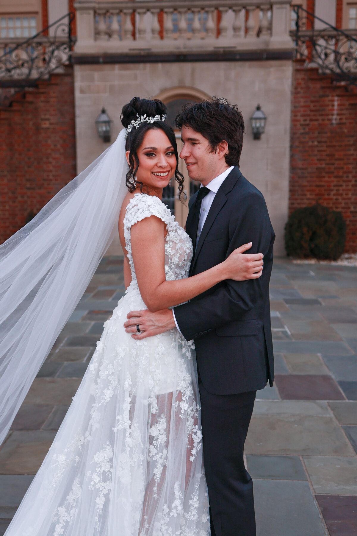 bride wearing a lace and while floral dress and groom wearing black suit while holding each other