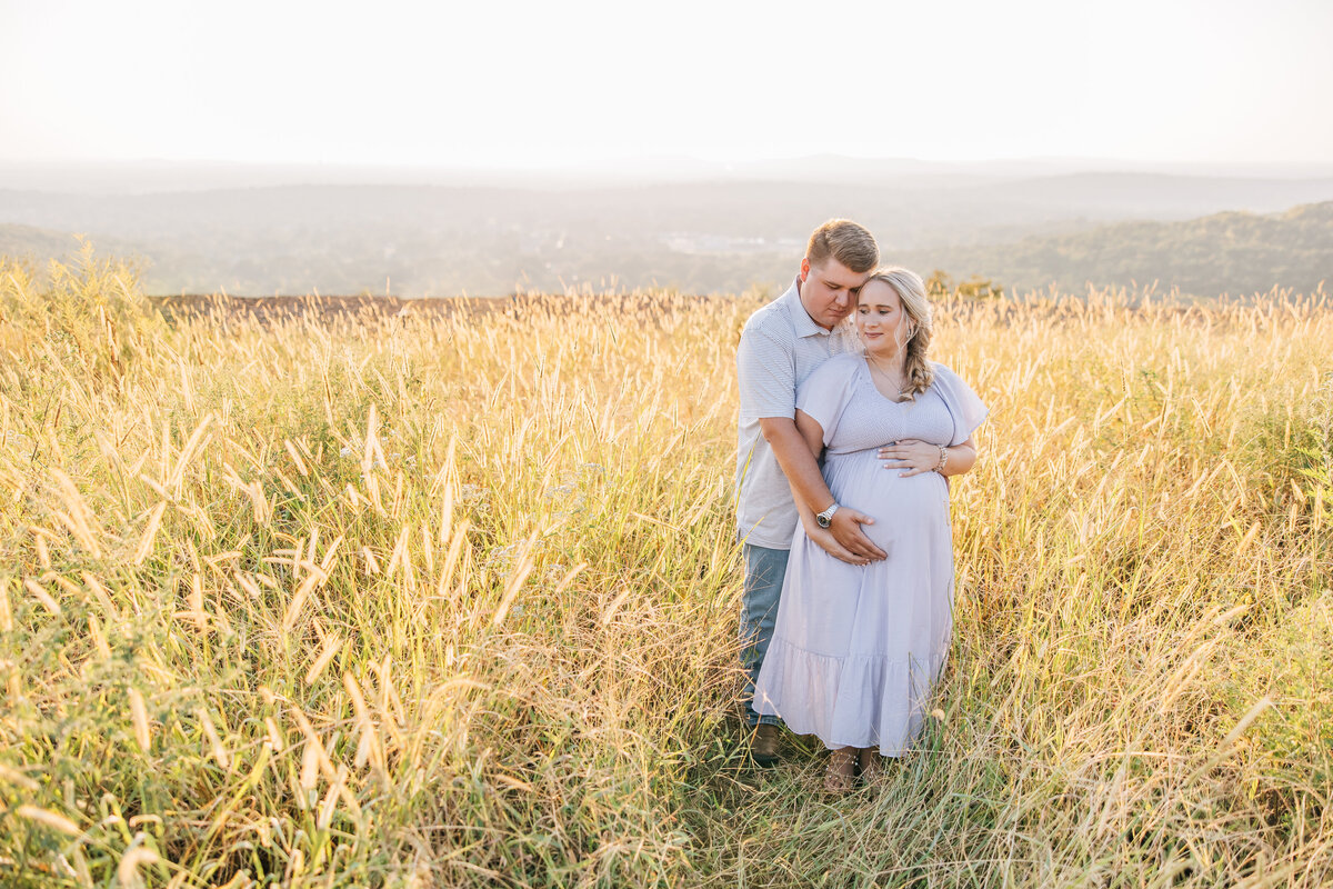 pregnant woman and man embracing in wheat field