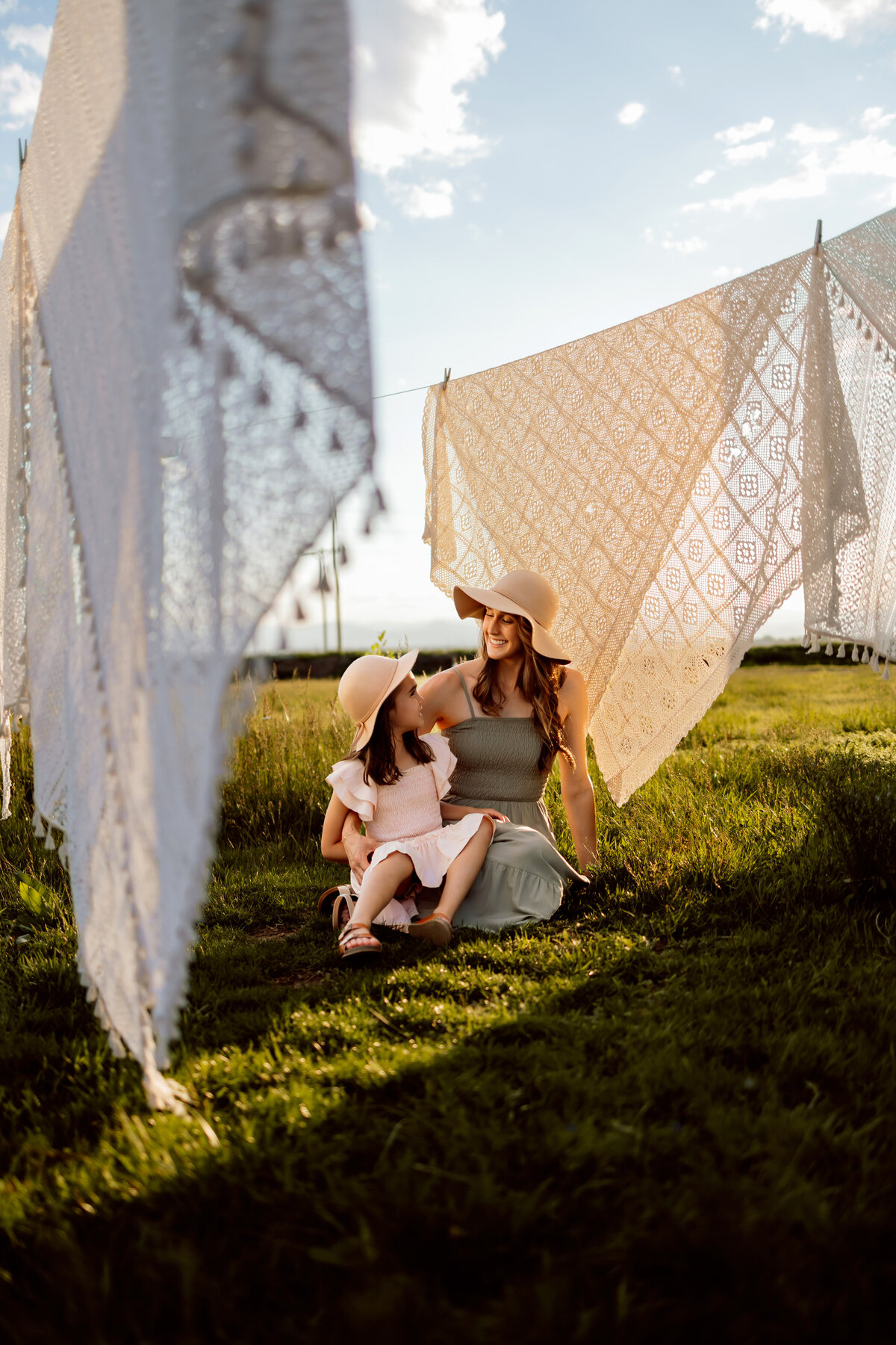 Mom and daughter sitting on a farm in the grass on a warm summer day near blankets drying on a clothing line