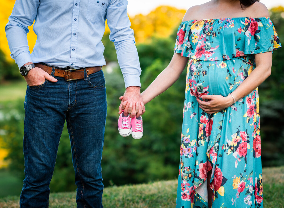 Pregnant couple holding baby shoes, sharing a joyful moment outdoors