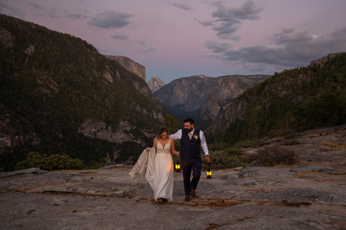 Bride and groom walk towards the camera holding lanterns as the sunsets on their California elopement day.