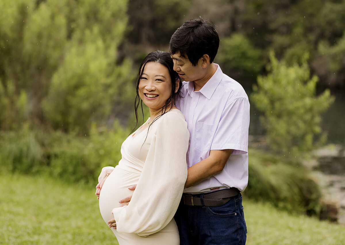 couple holding pregnant belly outside laughing