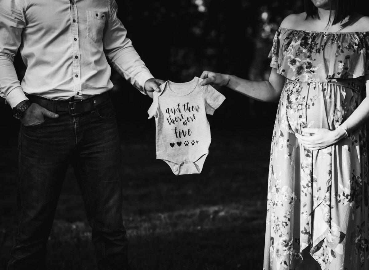Couple holds baby onesie, announcing their pregnancy