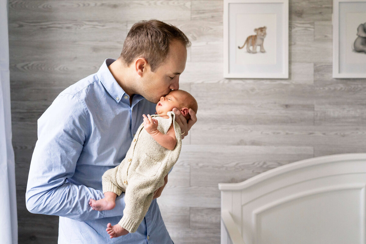 Father in blue shirt kissing newborn baby during Atlanta newborn photography session