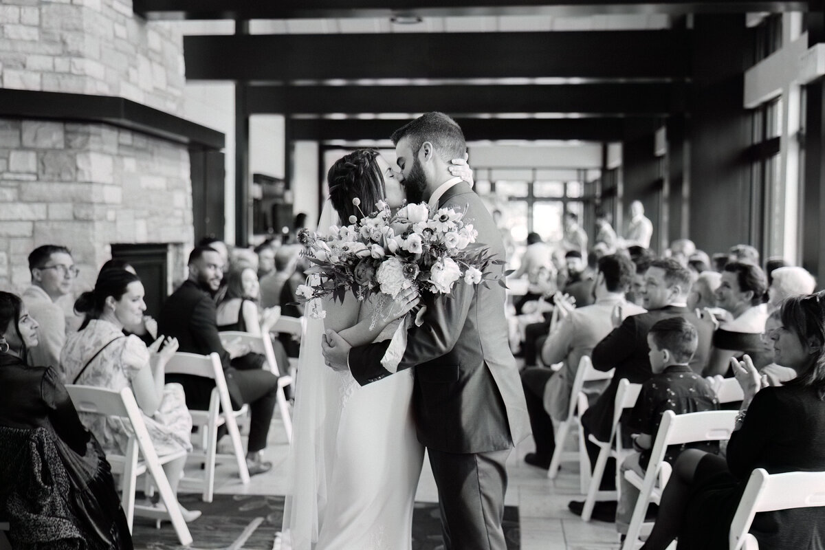 Black and white wedding portrait of the bride and groom's kiss at the end of the altar