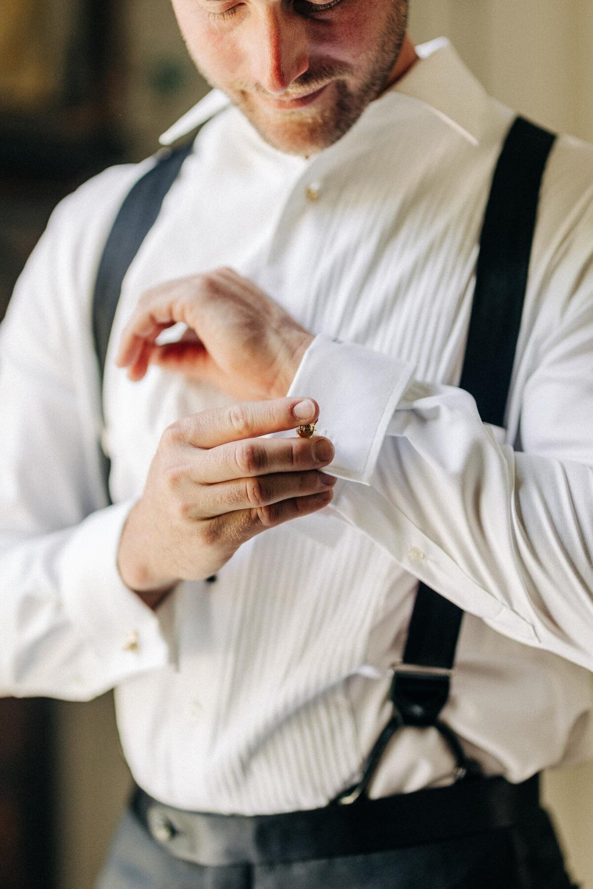 Man in a white shirt and suspenders adjusting his cufflink.