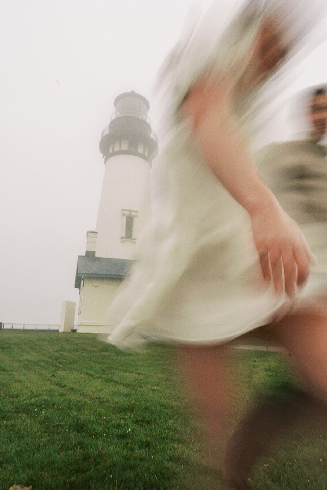 A blurry image of a couple running with a foggy lighthouse in the background. 