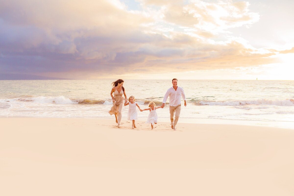 Young family holds hands and runs toward Love + Water Photography's camera during a beach portrait shoot in Wailea