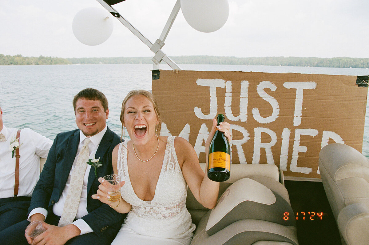 couple popping champagne in front of a cardboard just married sign