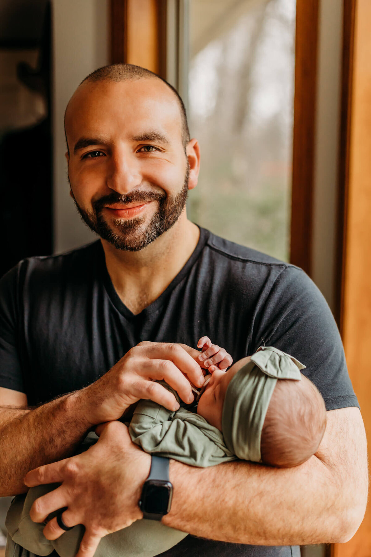 happy dad holding newborn near window with luci levon photography