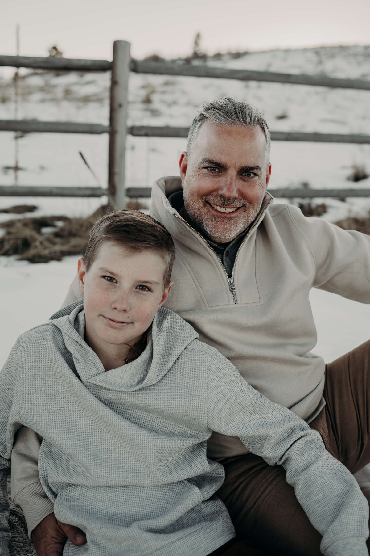 A portrait of a father and son, smiling towards the camera, wearing matching sweaters during a winter family photography session.