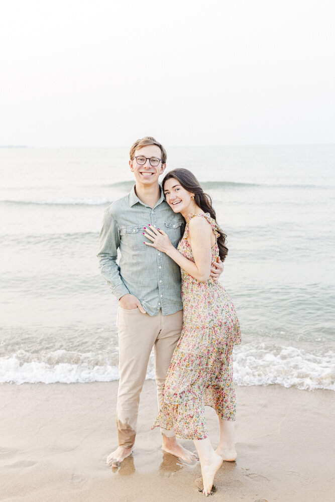an engaged couple hugging and smiling with the ocean in the background