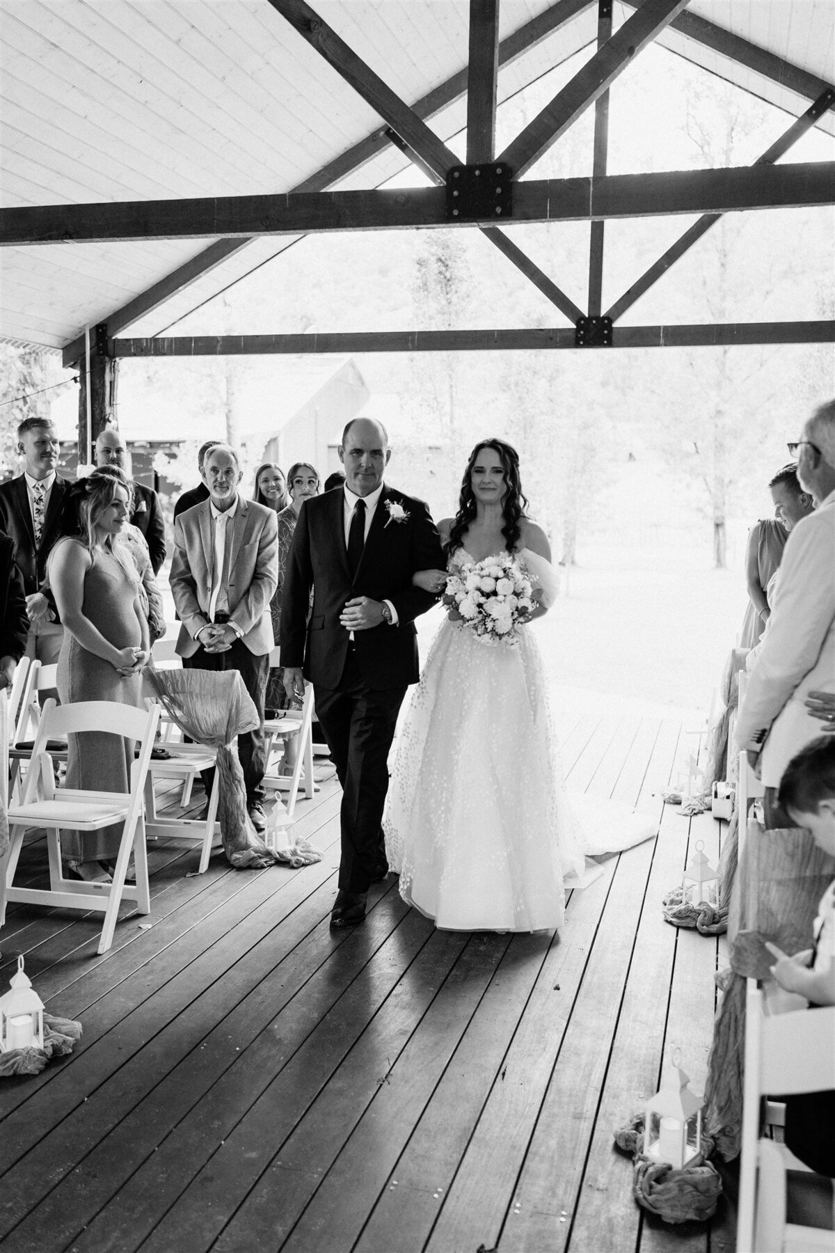 A radiant bride, her hand gently clasped in her father's, glides down the aisle, her eyes gleaming with anticipation and joy.